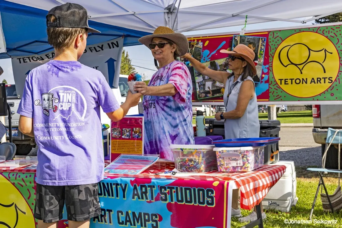 Young volunteer and community members at a Teton Arts nonprofit booth during the Tin Cup Challenge